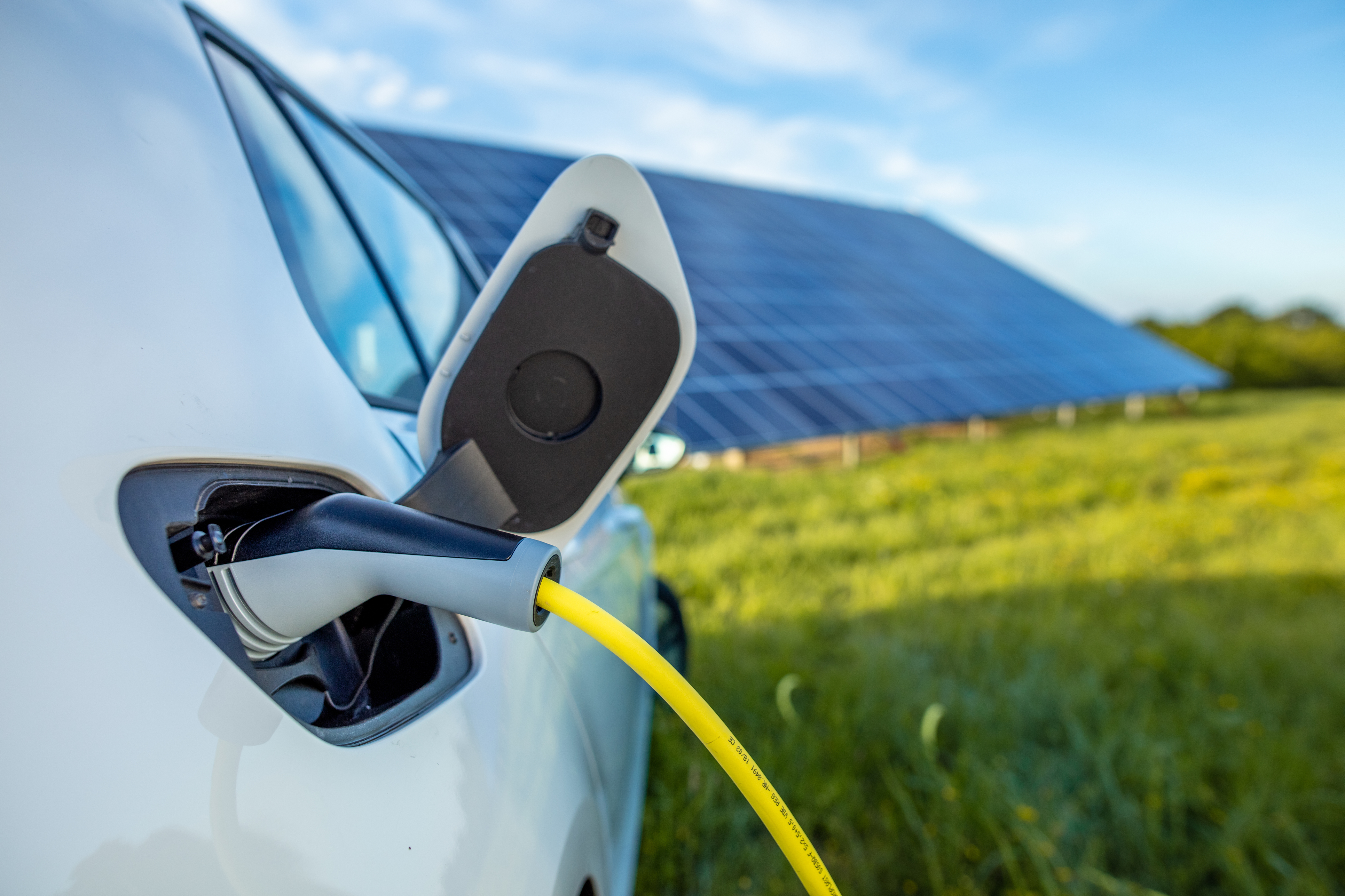 Close up of electric car charging in field with solar pannels in the background 